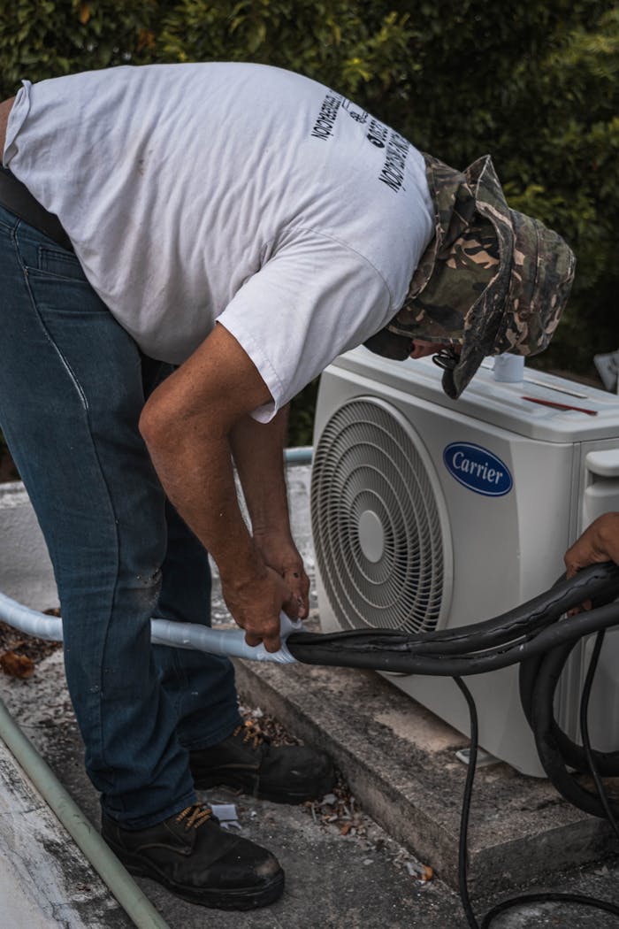 creative A technician performs maintenance on an outdoor air conditioning unit, focusing on hose connections.
