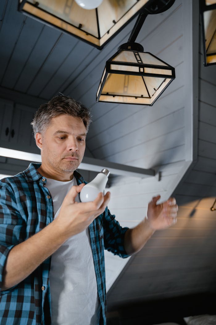 creative-03 Man in a plaid shirt replaces a light bulb in a modern, stylish home interior.